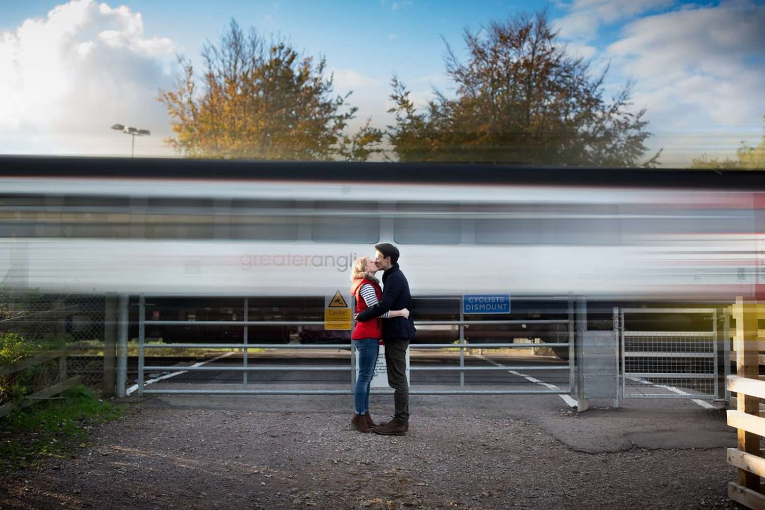 An engaged couple stand and hug in front of a speeding train at Woodbridge in Suffolk 
