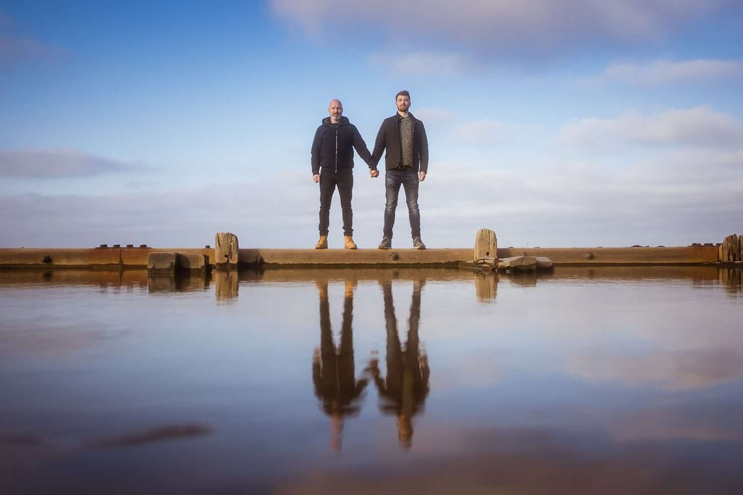 A same sex couple pose for an engagement shoot at Cart Gap beach in norfolk 

