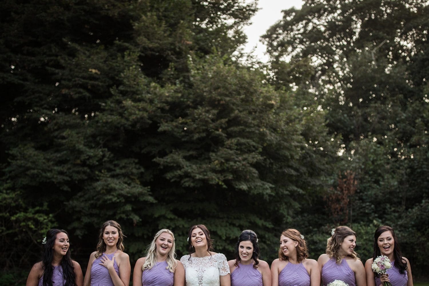 A bride and her bridesmaids giggle at a formal photo at the wedding.  Milsoms Kesgrave Hall wedding