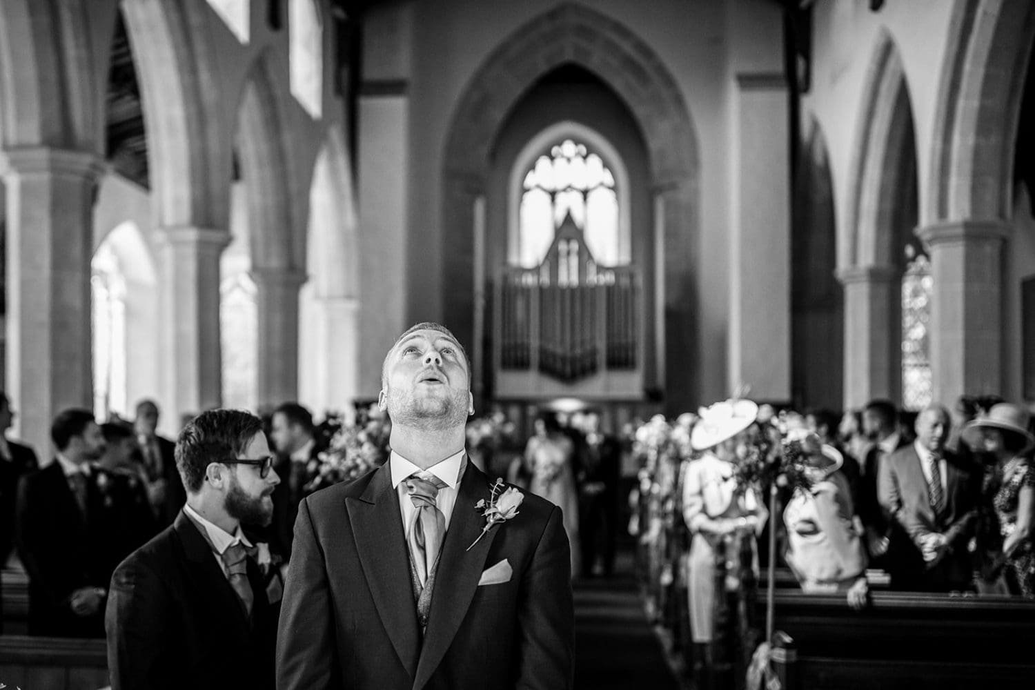 groom looks up to the sky as he nervously awaits his bride at their suffolk wedding