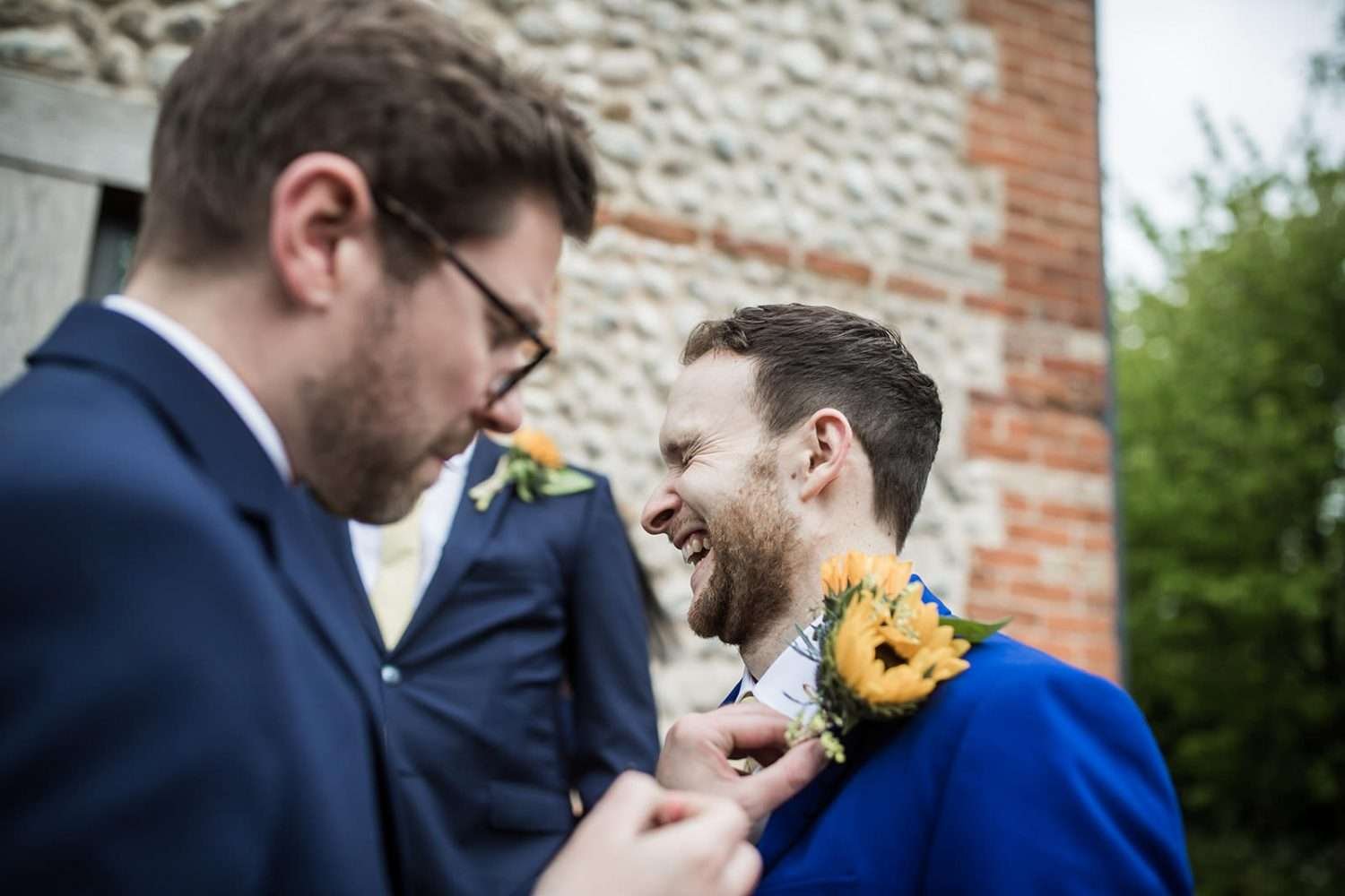 Groom has his buttonhole atached whilst preparing for his wedding at chaucer barn in norfolk 