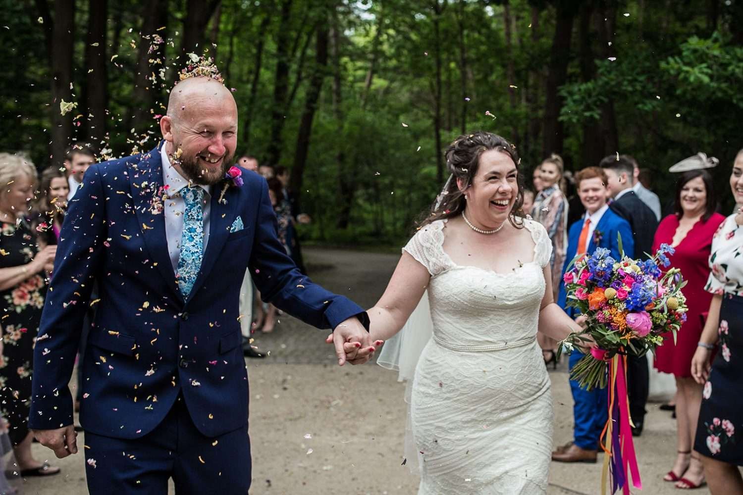 Bride and Groom smile and laugh while walking through their guests who are throwing confetti after their wedding ceremony at Greenacres wedding venue Colney Norwich Norfolk. 
