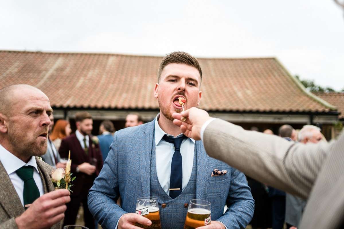 A guest is fed a canape by a friend whilst others look on at this Easton Grange wedding reception. 

