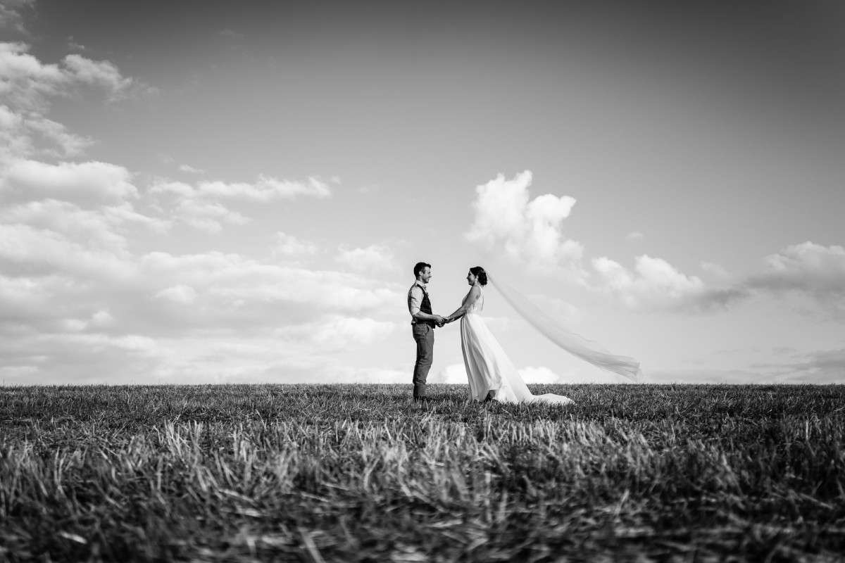 Bride and groom standing and holding hands in a large recently harvested field at their suffolk wedding.