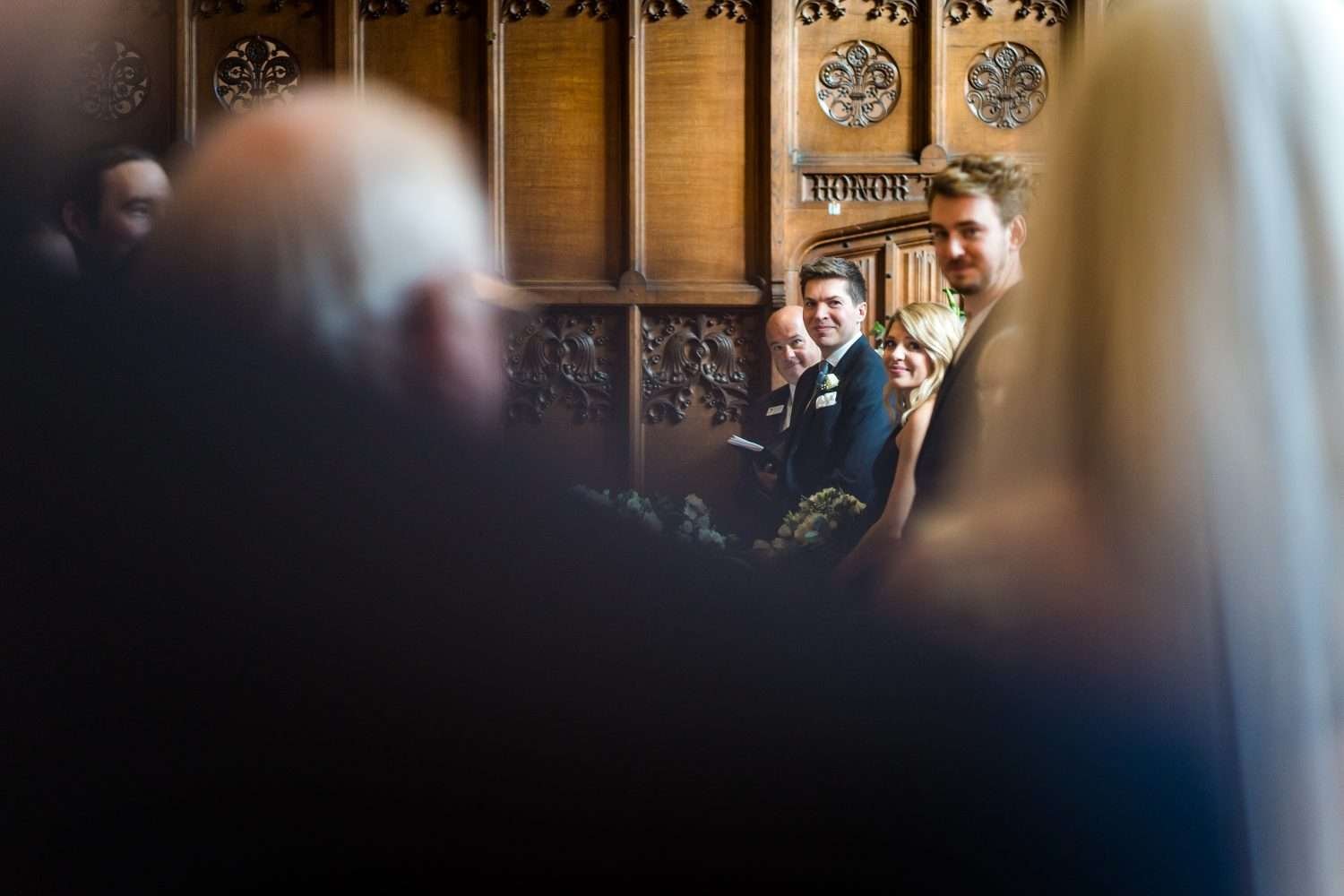 A groom looks up the aisle as his bride arrives to their wedding ceremony escorted by her father. 