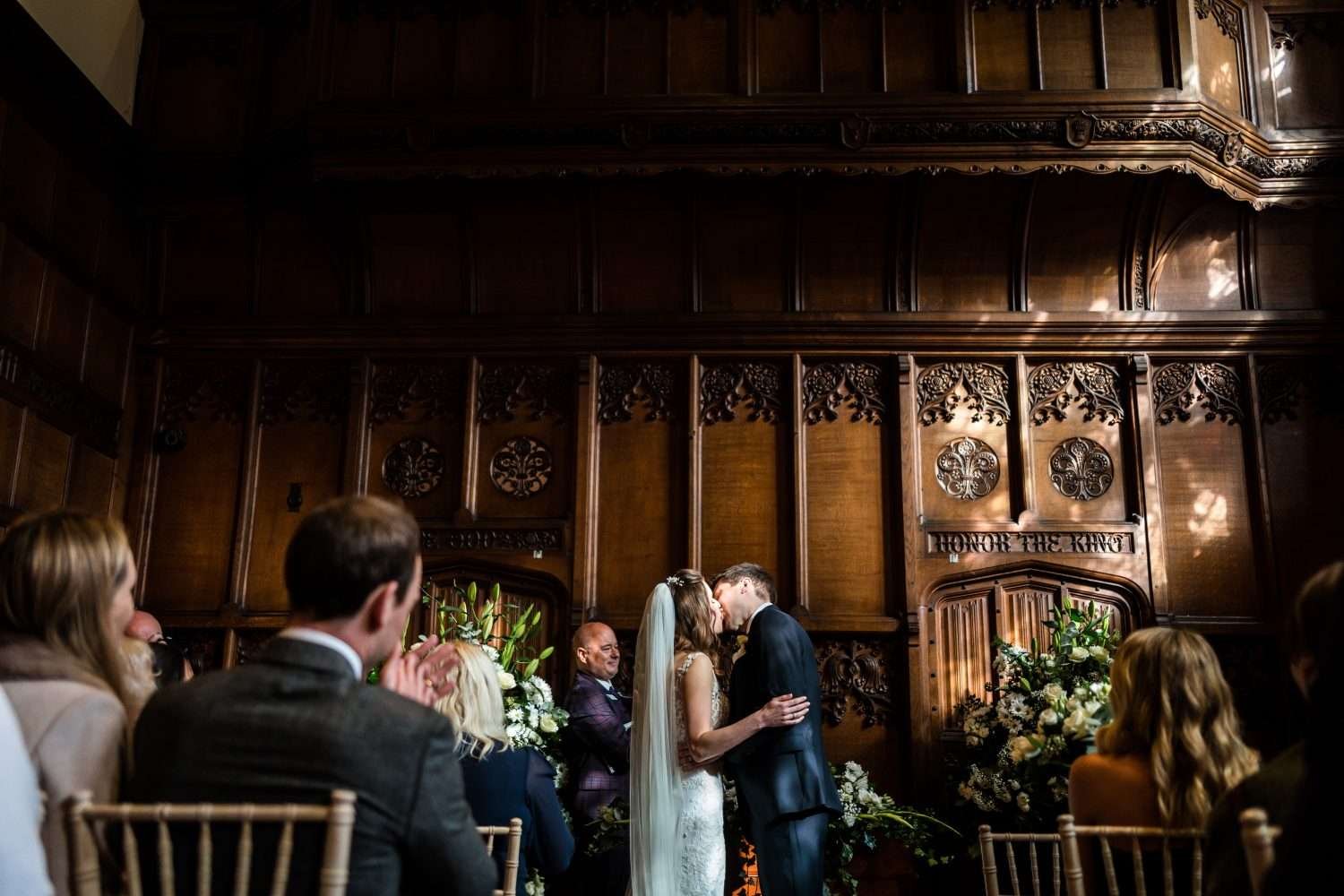 A bride and groom kiss as their wedding ceremony comes to an end in a sunlight wood panelled elizabethan room at hengrave hall in suffolk
