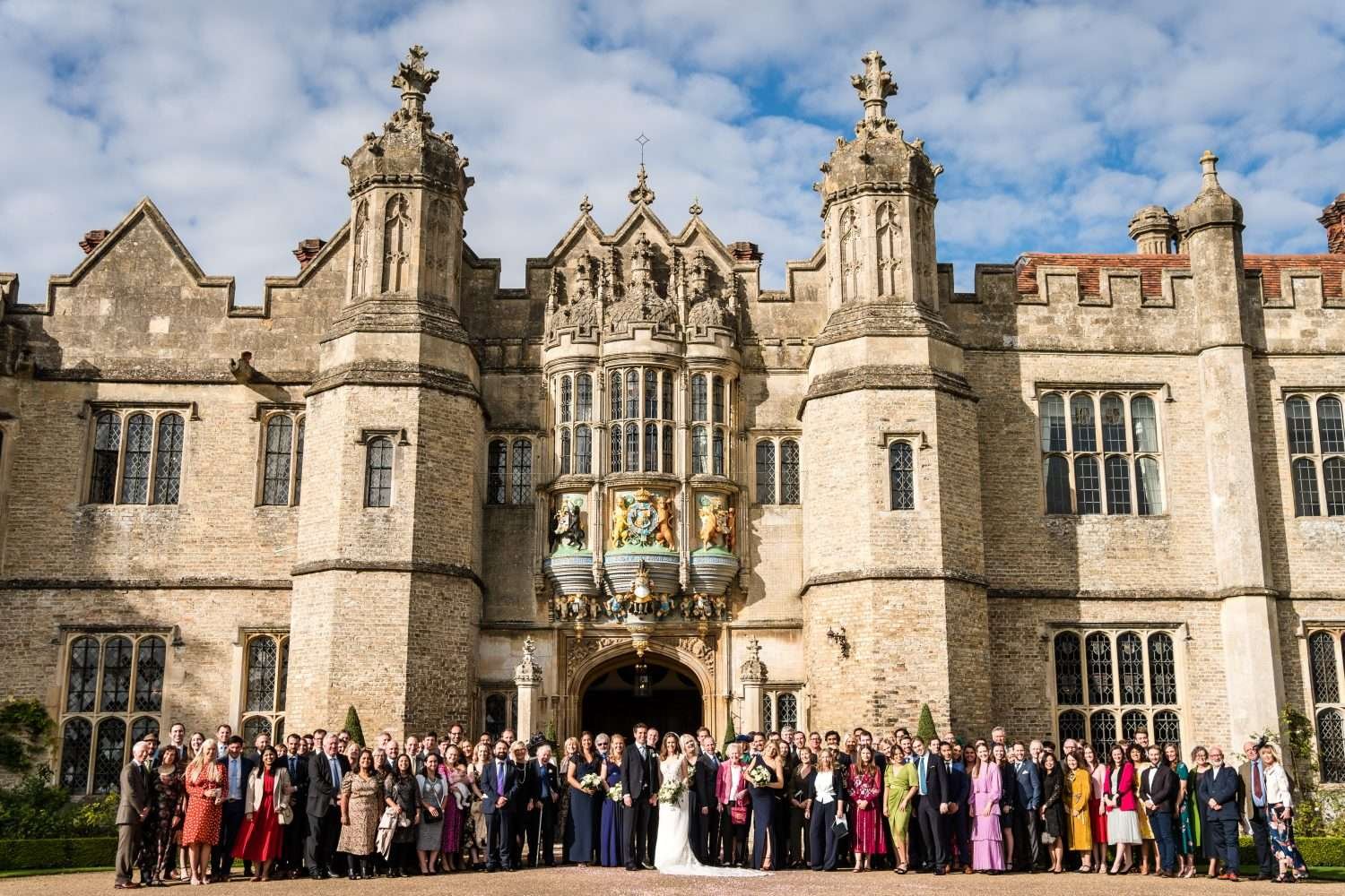 A very large group shot of the family and guests at a wedding . Taken in sunshine at the front aspect of hengrave hall in suffolk. 