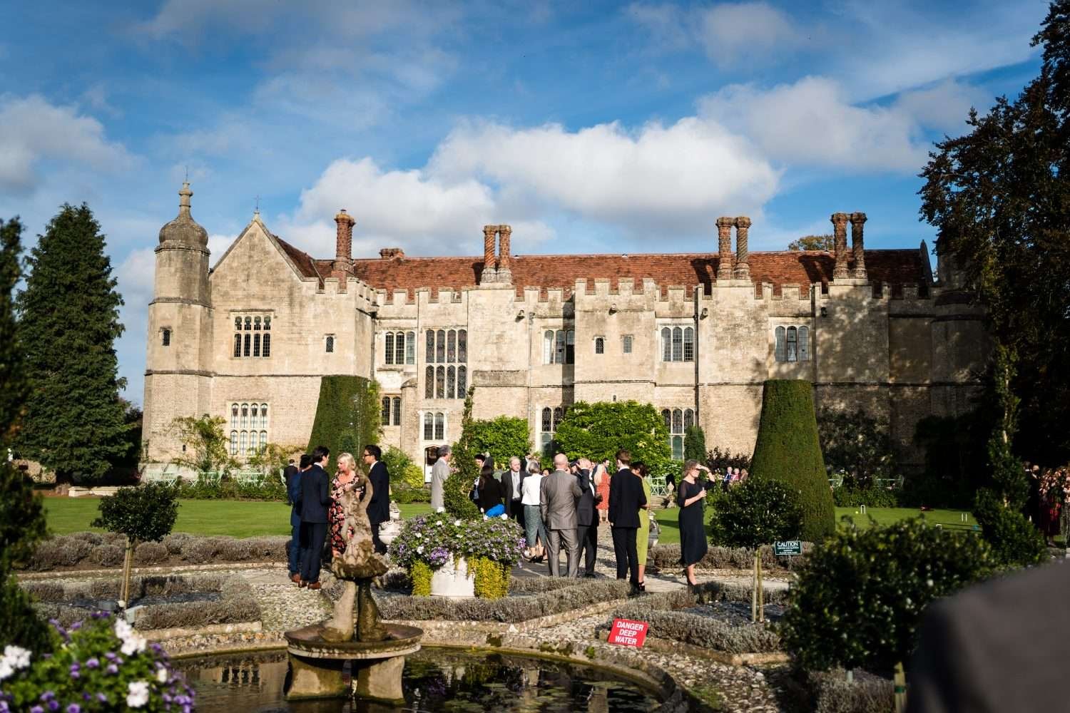 wedding guests enjoying a drinks reception in october sunshine on the west terrace at hengrave hall in suffolk 
