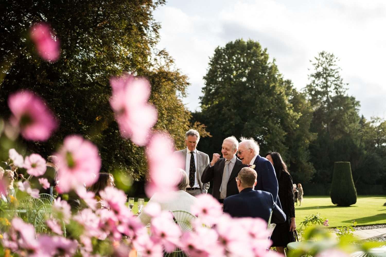 guests enjoying autumn sunshine of the west terrace at hengrave hall in suffolk at a wedding. 
