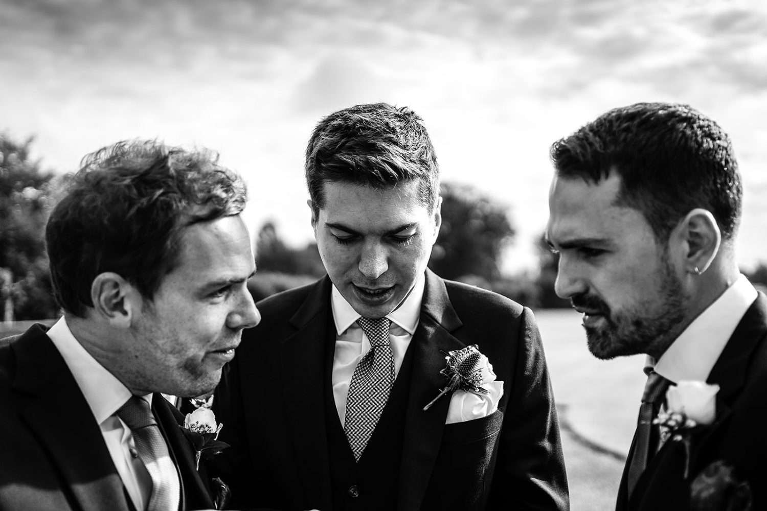 A sunny morning and a Groom looks down to check a list of details for his wedding day. To his left and right, in the front of the frame are his best man and usher who are also discussing details of the day. They all look a little concerned and occupied!