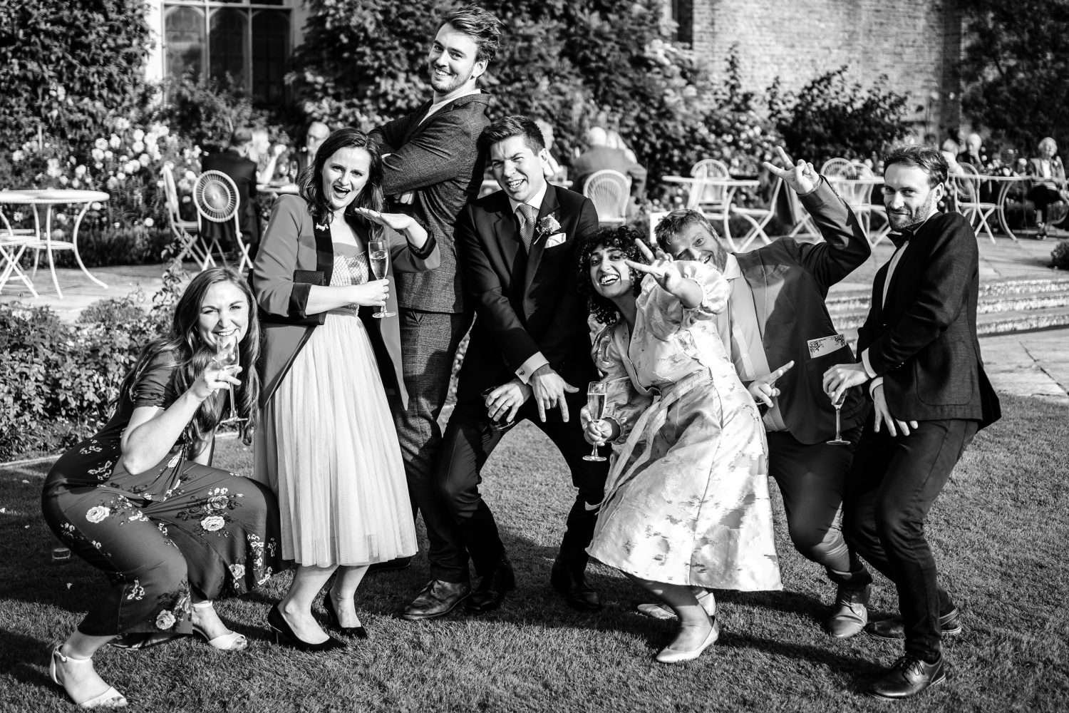 A groom on his wedding day, surrounded by his friends. Everyone is striking a funny pose and all are laughing.