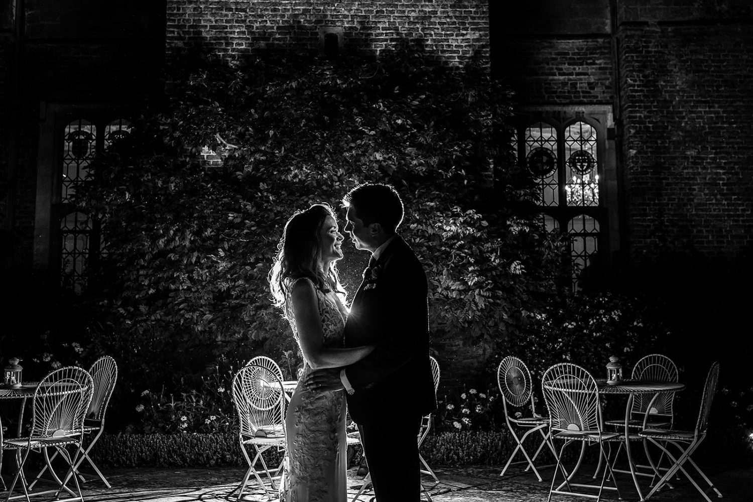 a black and white photo of a bride and groom chest to chest and illuminated by a flash light behind them. They are stood on the west terrace at their hengrave hall wedding. 