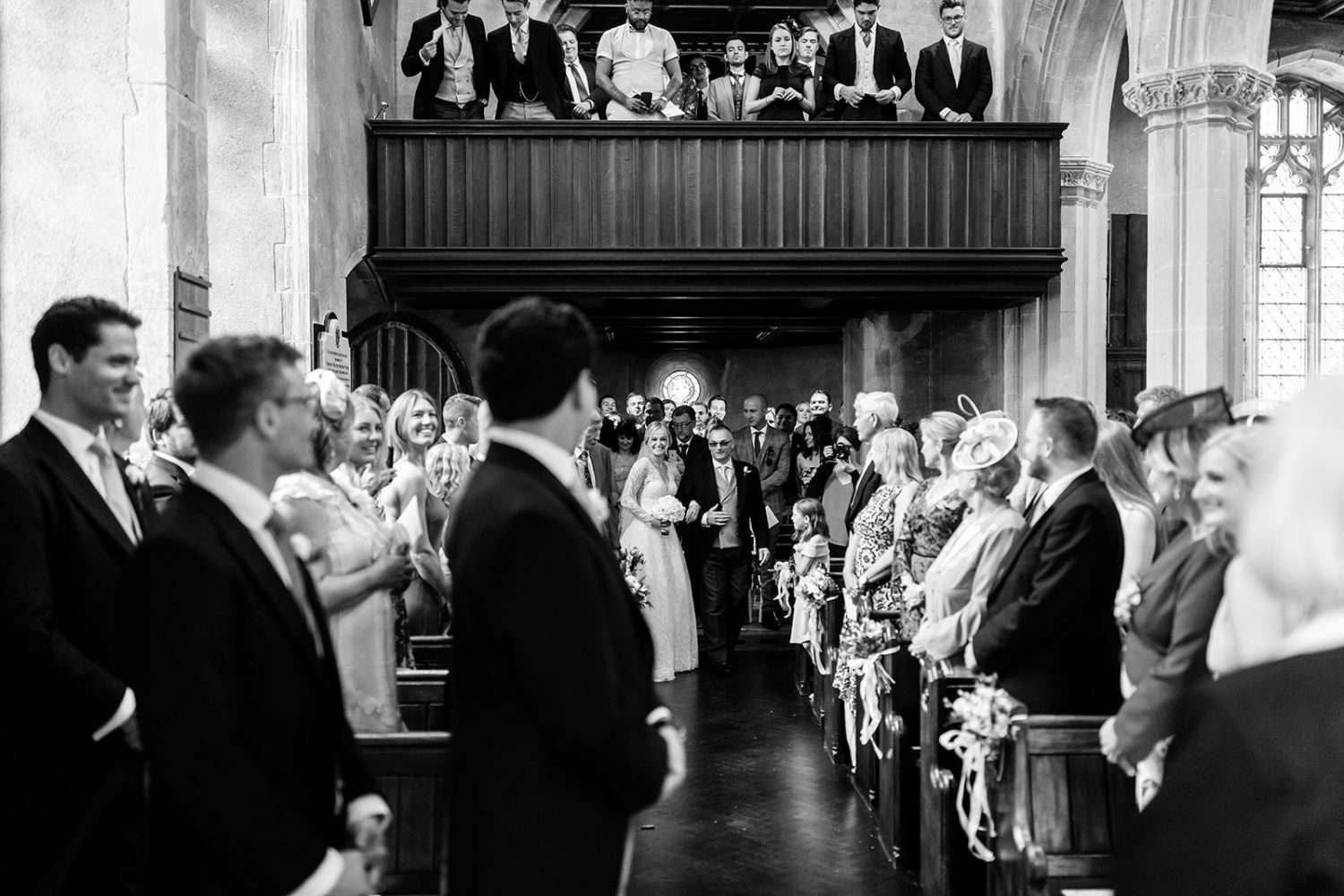 A black and white photo from a wedding in Suffolk at Hengrave hall. We see a Bride and her father as they come down the aisle at the Hall's little church at the start of the ceremony.  