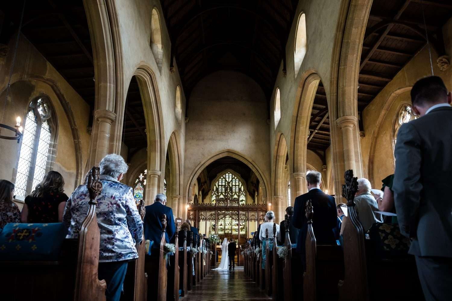 A long view down the aisle of an english church as a bride and groom exchange vows during their ceremony in norfolk. An example of 'how do wedding ceremonies work'. 