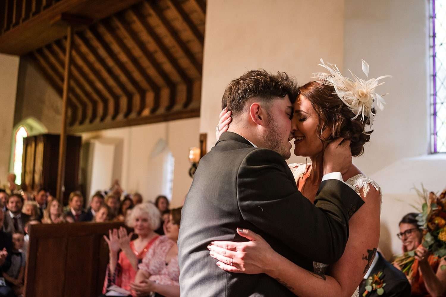 A bride and groom have their first kiss at the end of their wedding ceremony at the church at fishley hall in the norfolk broads. Their family watch on and applaud. 