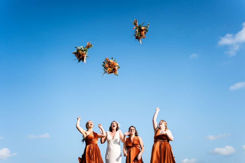 Bride and her Bridesmaids throw their bouquets into the air at a Fishley Hall wedding in the Norfolk Broads. 