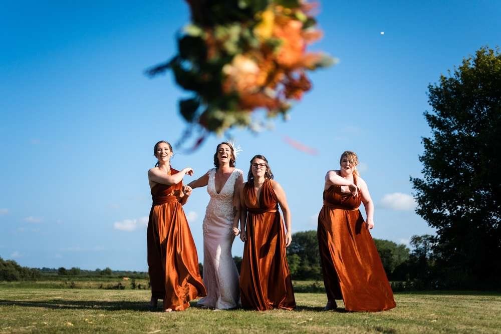 Bride and her Bridesmaids throw their bouquets into the air at a Fishley Hall wedding in the Norfolk Broads. 