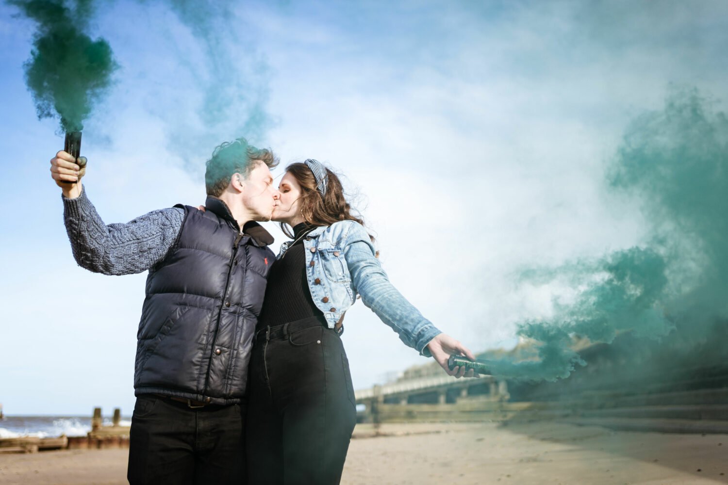 a newly engaged couple celebrate with a kiss at cart gap beach in norfolk, they are both holding green smoke bombs