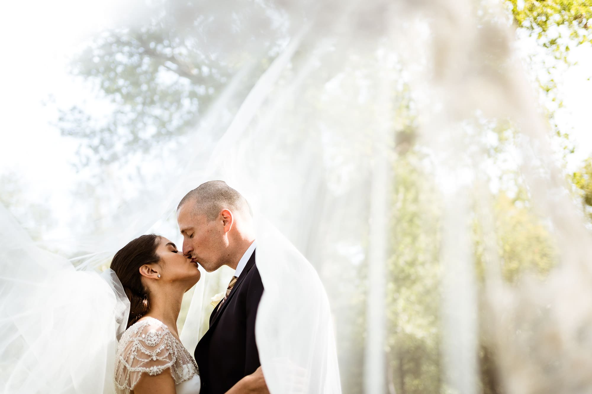 A bride and Groom kiss under the Bride's white veil