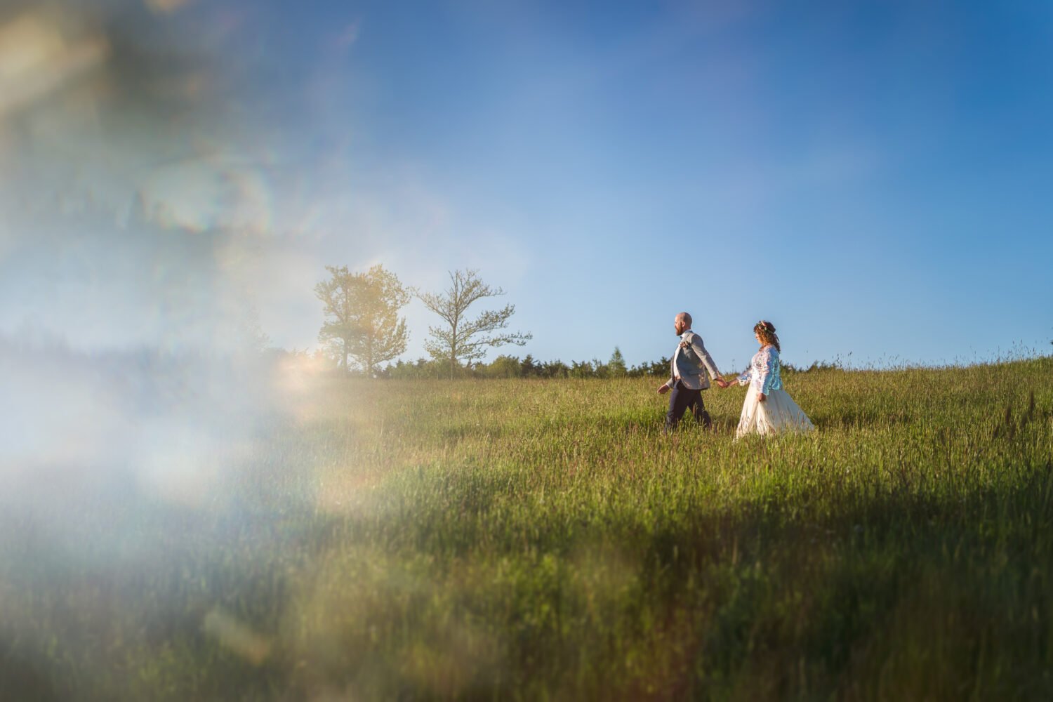 Couple walk across the meadow in the evening at their Chaucer Barn wedding in Norfolk 