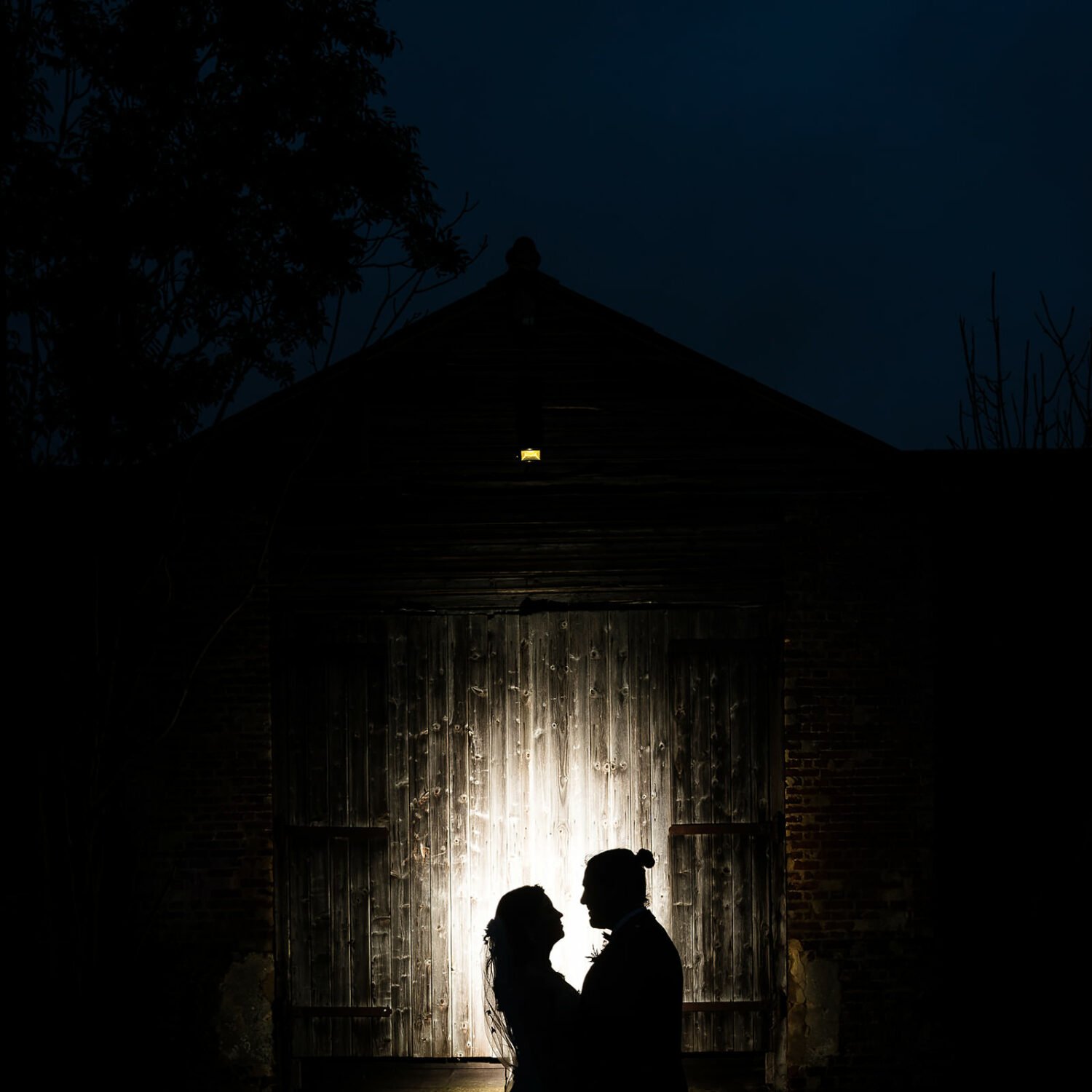  a couple portrait in front of the barn , it is evening and the couple are lit from behind by flash light. 