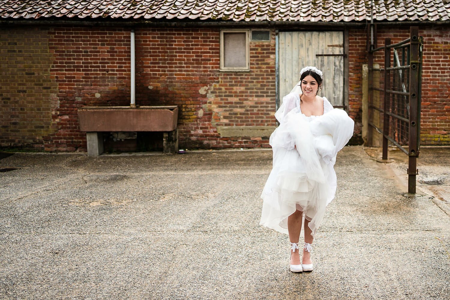 bride holds her dress in the cattle yard at fishley hall