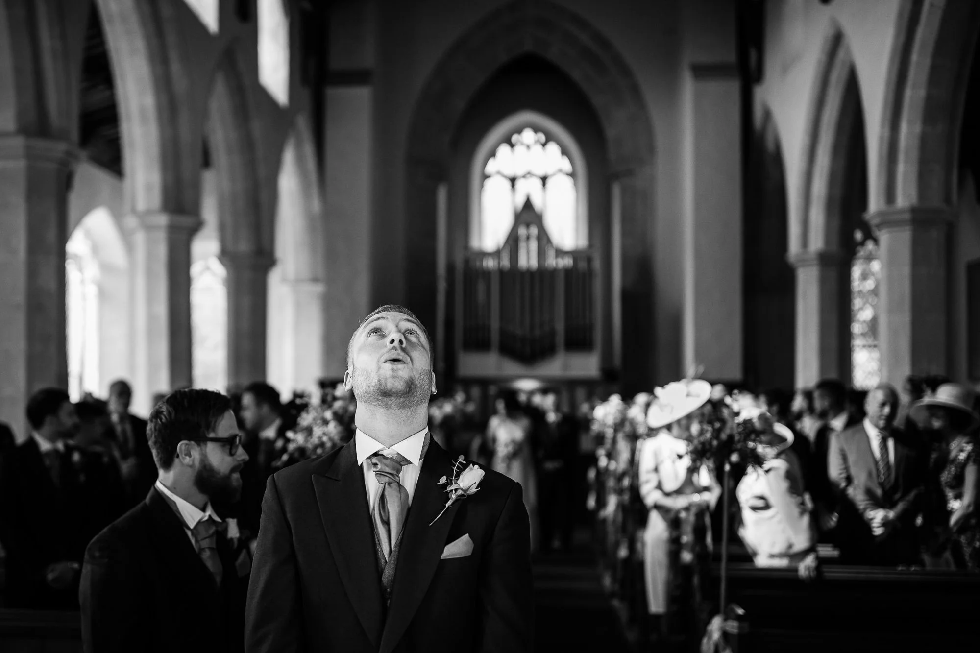 A Groom takes a deep breathe in a Church as the Bride walks down the aisle behind him. Black and white photo.