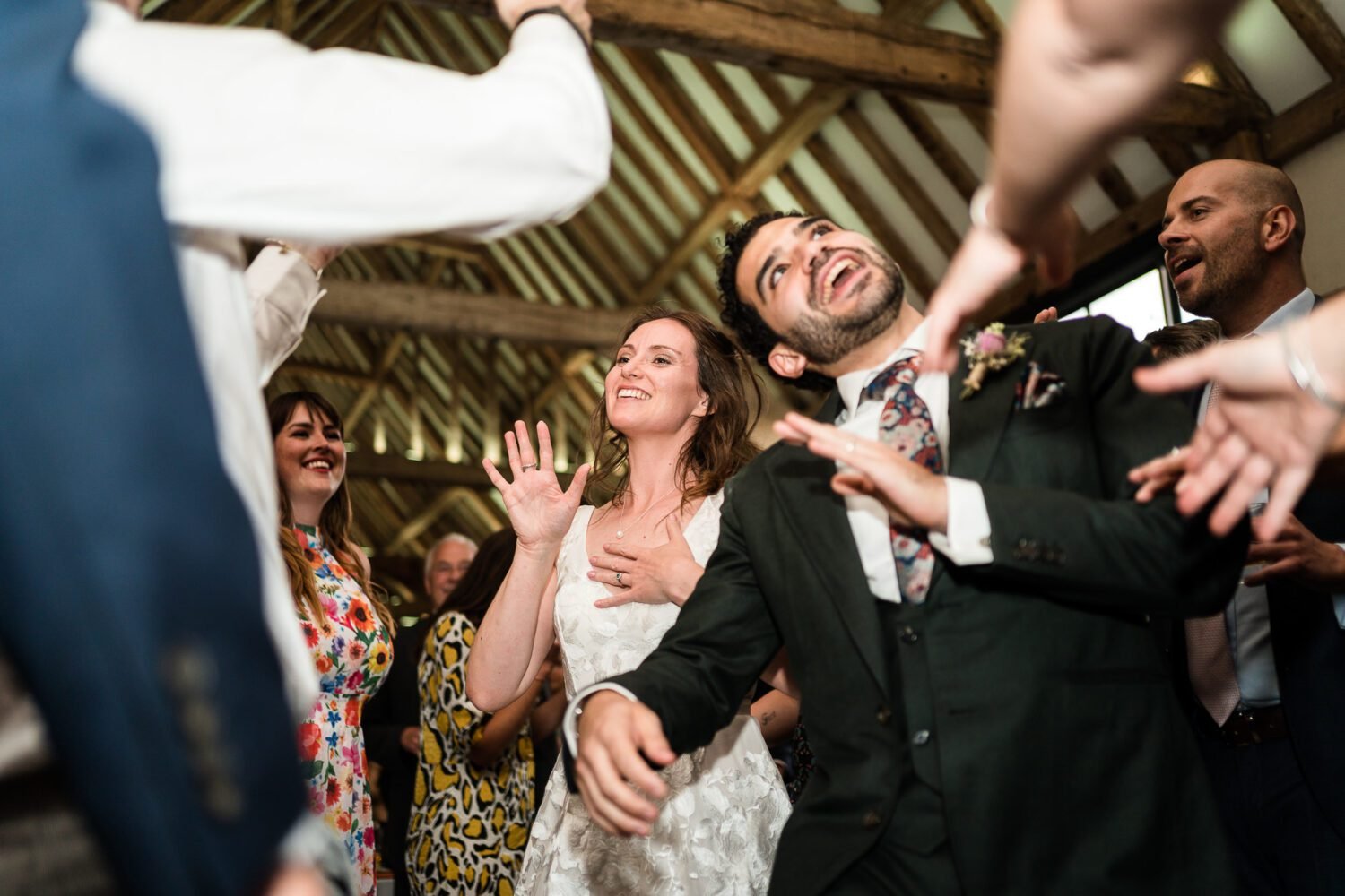 Bride and Groom are dancing together in a Norfolk barn and smiling whilst their guests watch