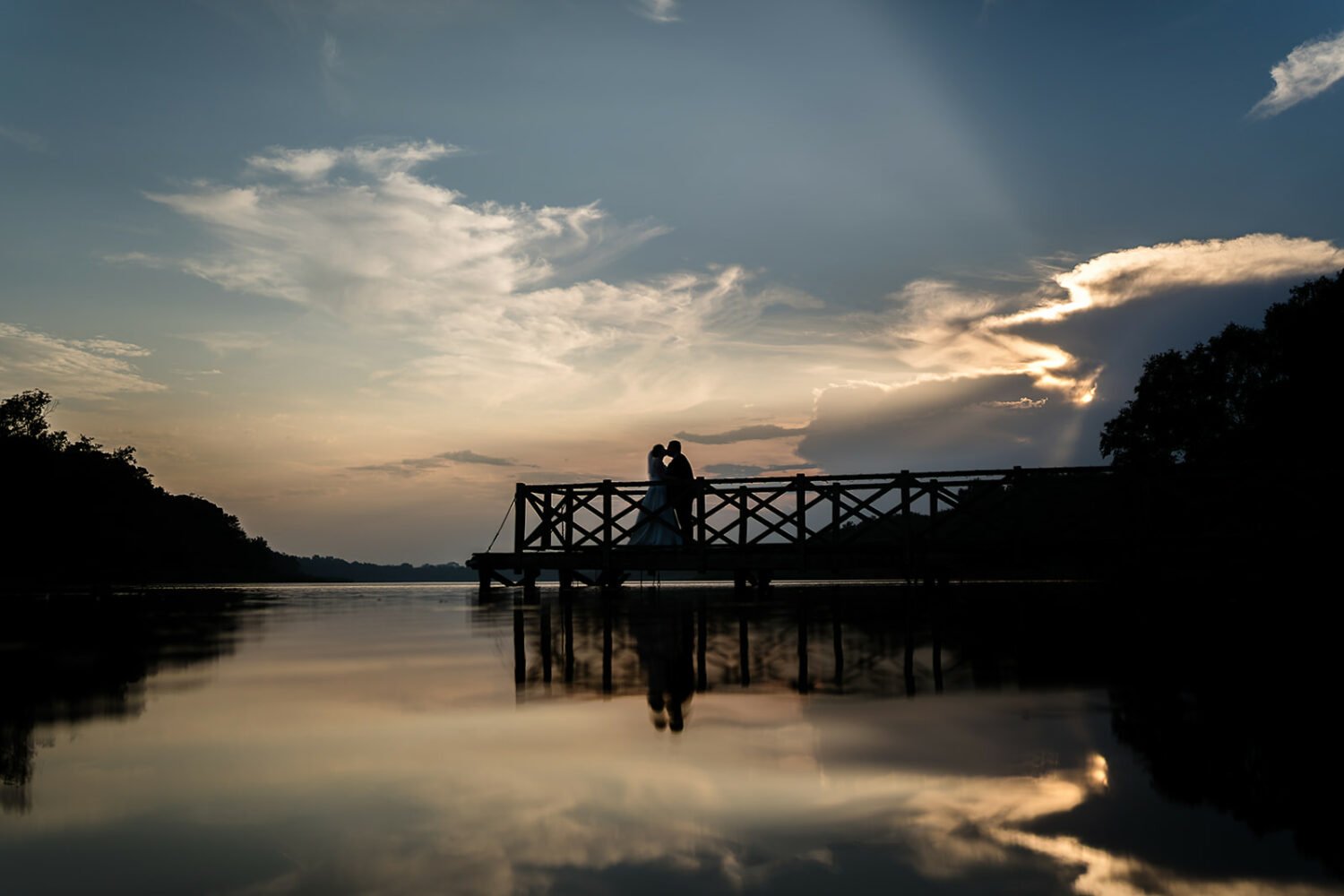 a wedding couple kiss on the jetty at the boathouse ormesby at sunset, they are in silhouette
