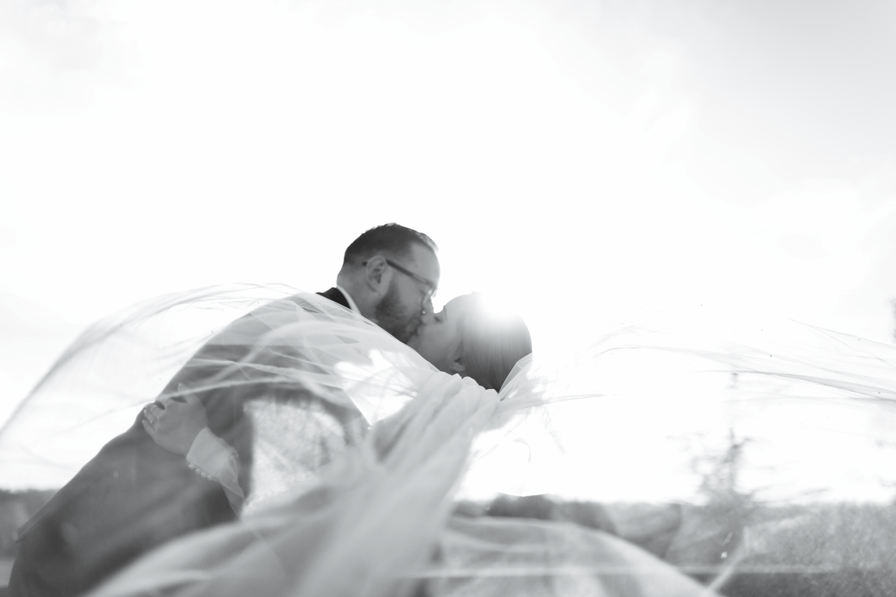 At sunset a bride and groom hug as the groom dips his new wife and her veil floats in the wind, they are happy and smiling. The wedding is a t kimberley hall in norfolk
