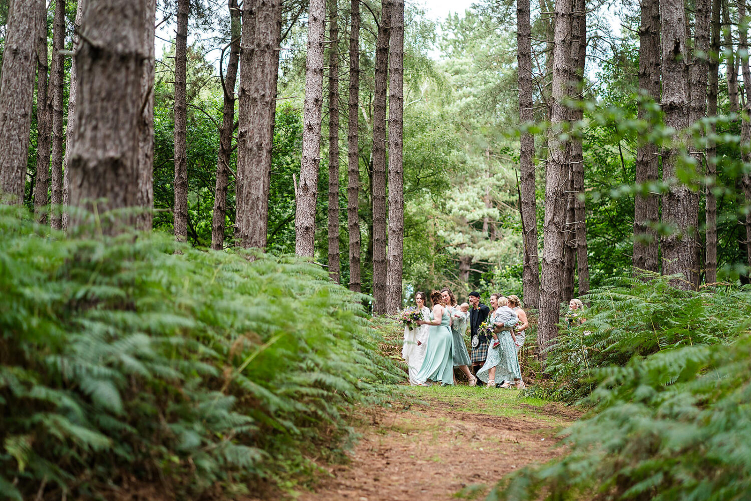bride and her party on their way to a woodland wedding ceremony at happy valley there are pine tress and Norfolk woodland all around