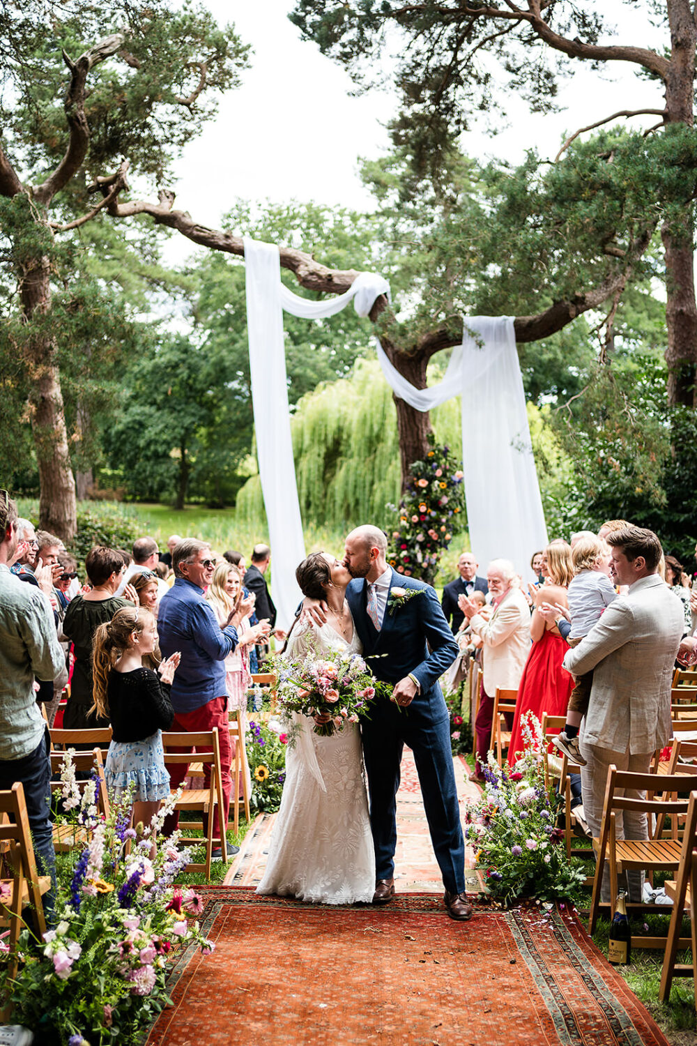 outdoors ceremony at happy valley in Norfolk, the couple have their first kiss in front of beautifully decorated woodland with a lakeside backdrop, by www.lisaandneil.co.uk
